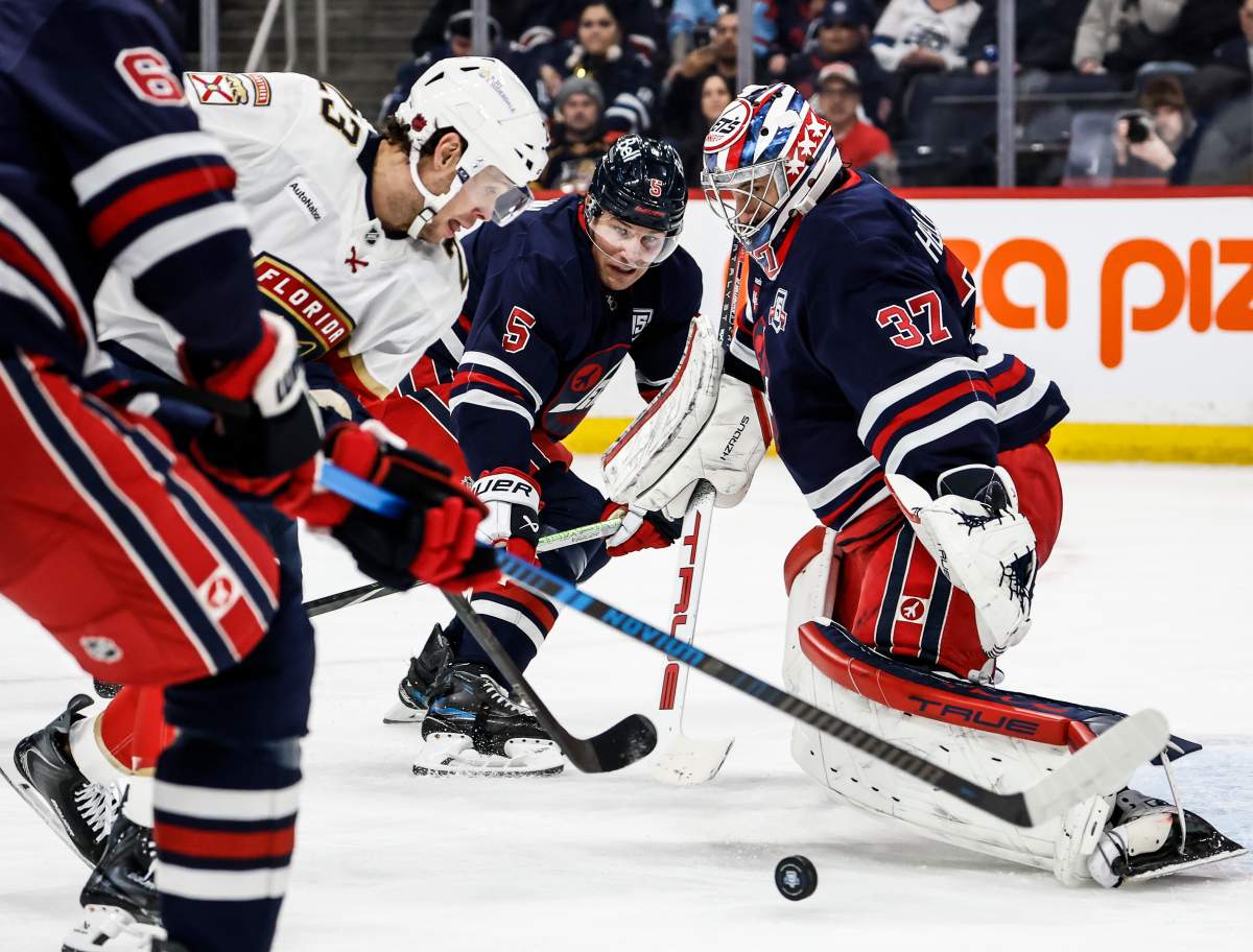 Florida Panthers' Carter Verhaeghe (23) makes a break for the net as Winnipeg Jets goaltender Connor Hellebuyck (37) and Luke Schenn (5) keep their eyes on the puck during first period NHL action in Winnipeg, Thursday, January 22, 2026. THE CANADIAN PRESS/John Woods.
