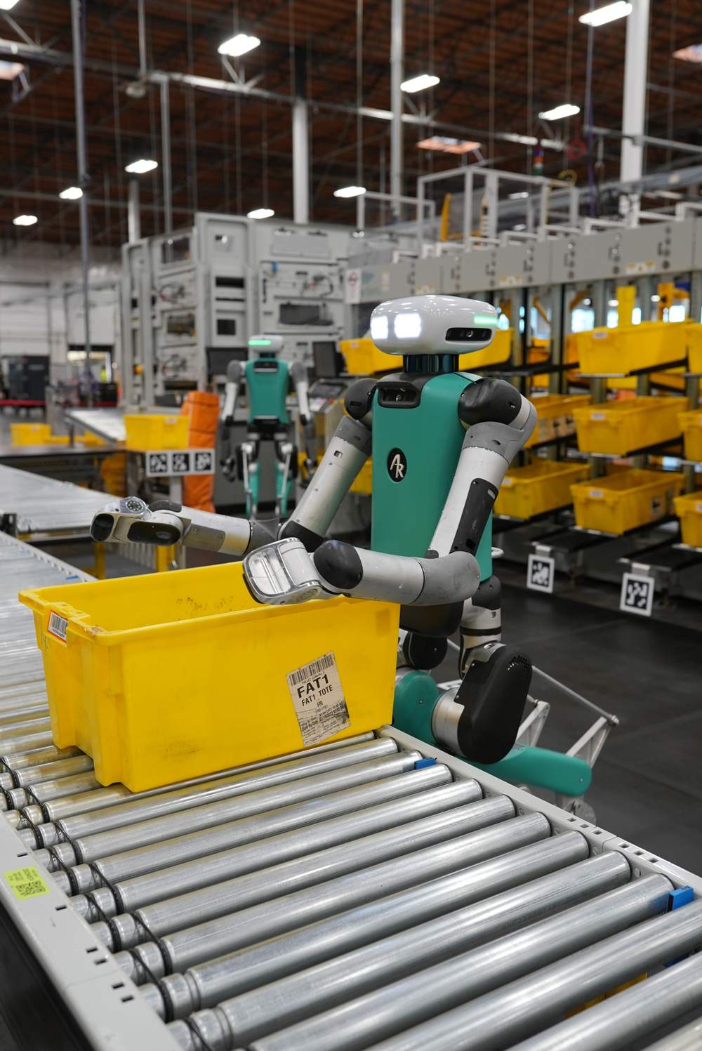 Digit, a humanoid robot developed by Agility Robotics, moves containers along a conveyor inside an Amazon facility.