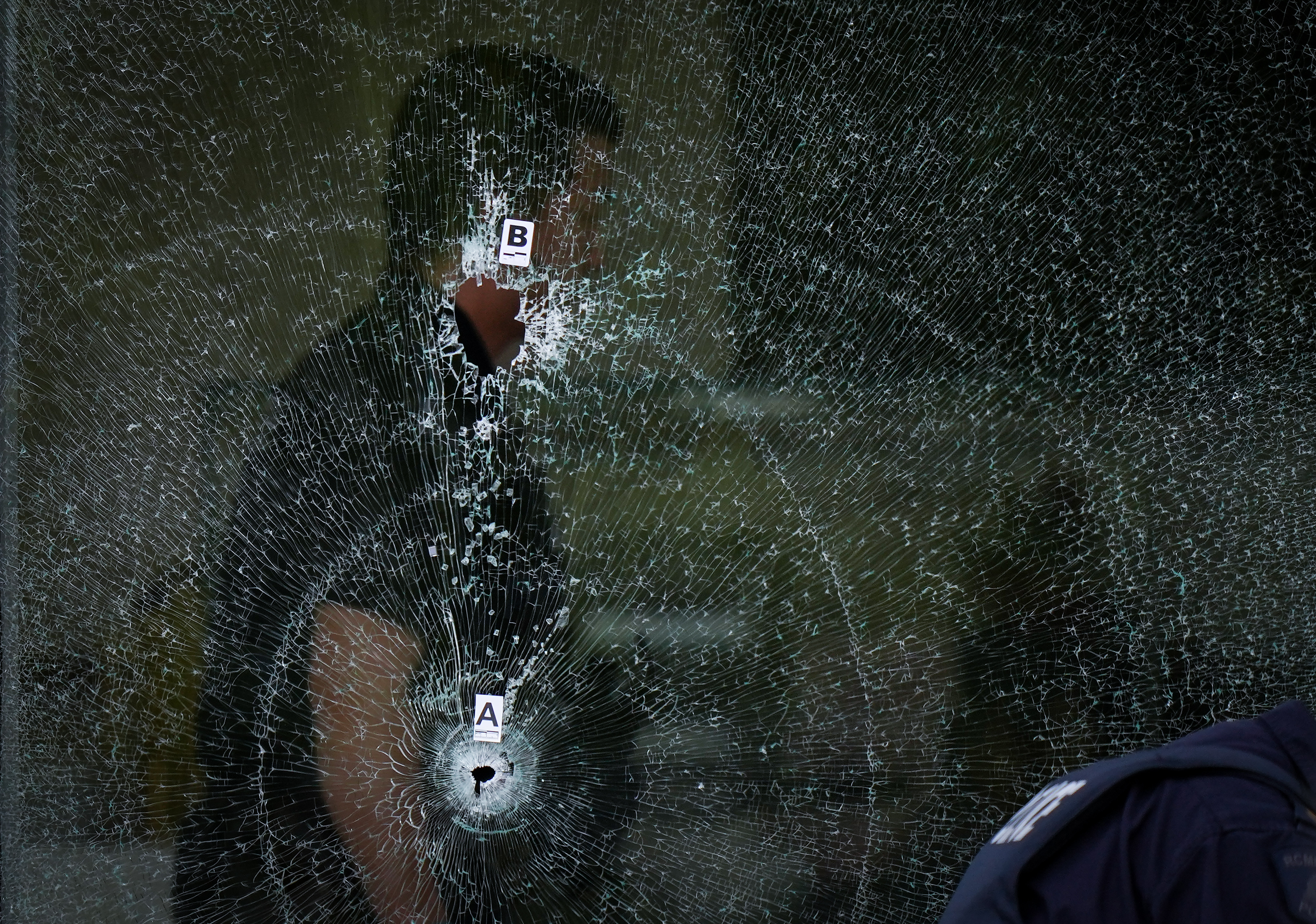 Bullet-holes in the window of a cafe as a police officer works inside, Surrey, B.C., Aug. 7, 2025.