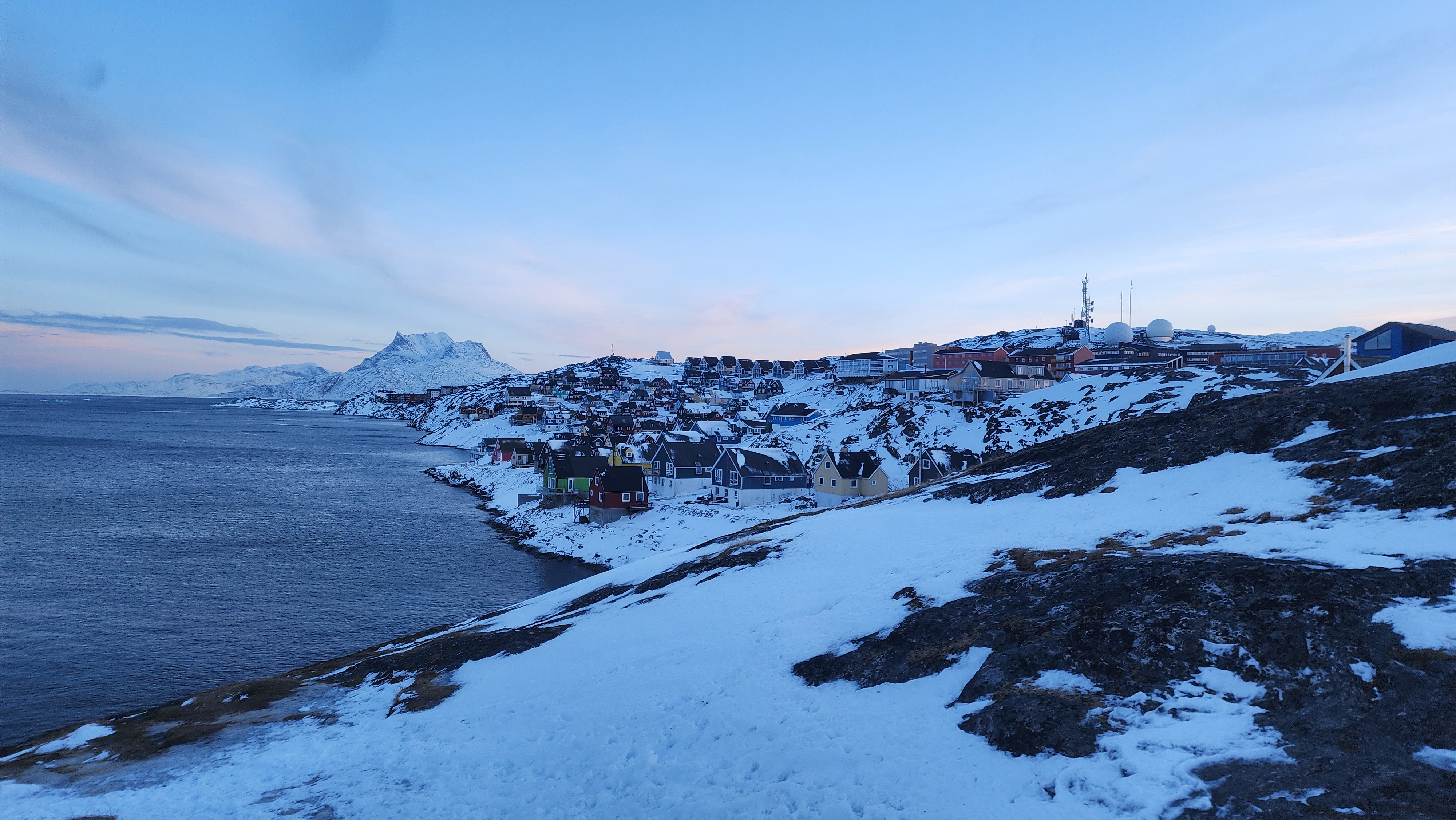 A snowy and rocky hillside is dotted with small colourful houses at dawn