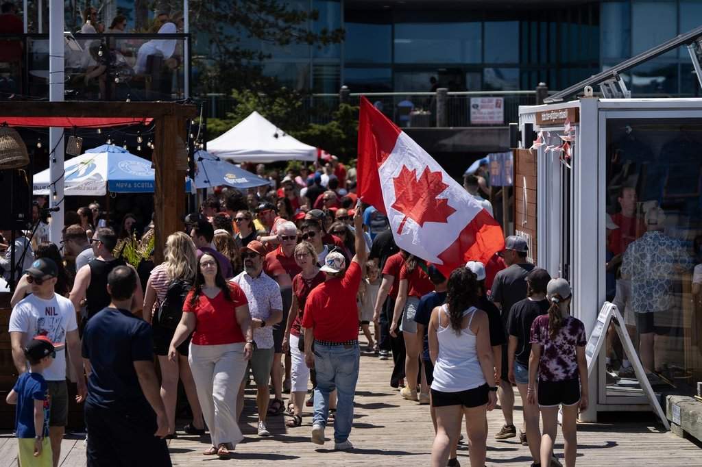 A reveller carries a Canada flag through a crowd on the Halifax Waterfront during Canada Day celebrations in Halifax, on Tuesday, July 1, 2025.  THE CANADIAN PRESS/Darren Calabrese.