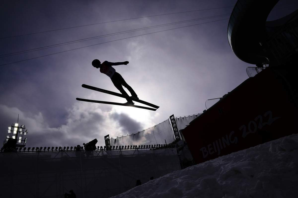 A trial runner soars through the air in silhouette at a ski jumping competition.