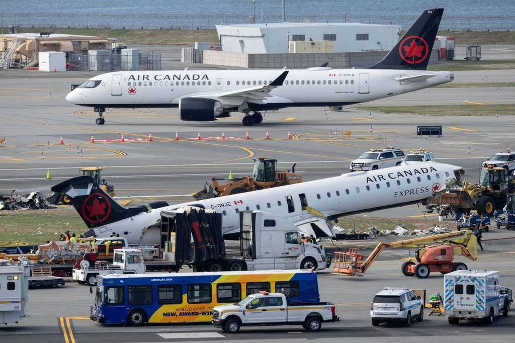 An Air Canada jet taxis past the wreckage of an Air Canada Express jet, Wednesday, March 25, 2026, as maintenance crews prepare to move the plane from the runway where it had collided with a Port Authority fire truck Sunday night at LaGuardia Airport, in New York. (AP Photo/Yuki Iwamura)