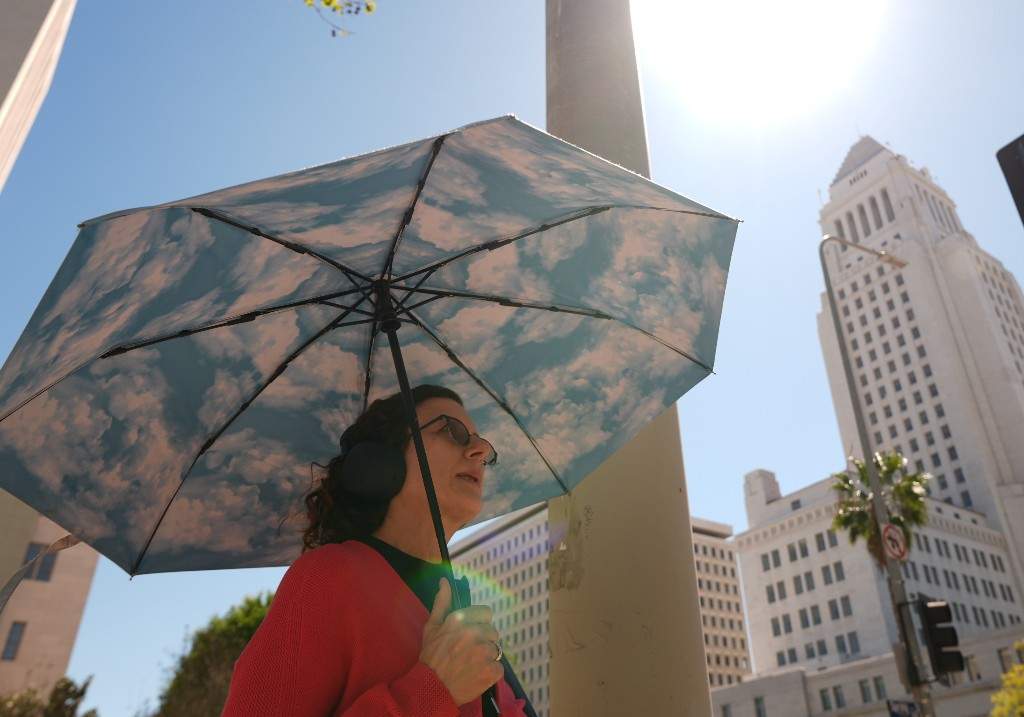 A pedestrian holds a cloud themed umbrella under a sunny day next to Los Angeles City Hall in Los Angeles Thursday, March. 12, 2026.