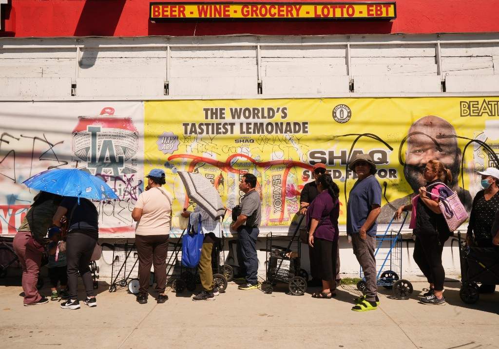 People cover themselves from the heat with umbrellas while waiting at a food distribution site Wednesday, March 11, 2026, in Los Angeles.