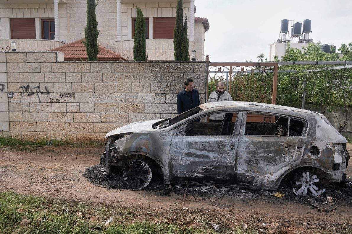 Palestinians inspect a torched vehicle next to a Hebrew graffiti on the sidewall that reads "revenge," following Israeli settlers' rampage through nearby Nablus-area villages on Sunday night, in West Bank village of Deir al-Hatab.