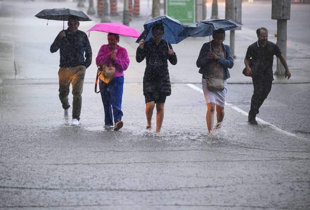 People hold umbrellas as they make their way through water pooling in an intersection as heavy rain pours down in Ottawa, on Thursday, June 6, 2024. THE CANADIAN PRESS/Justin Tang.