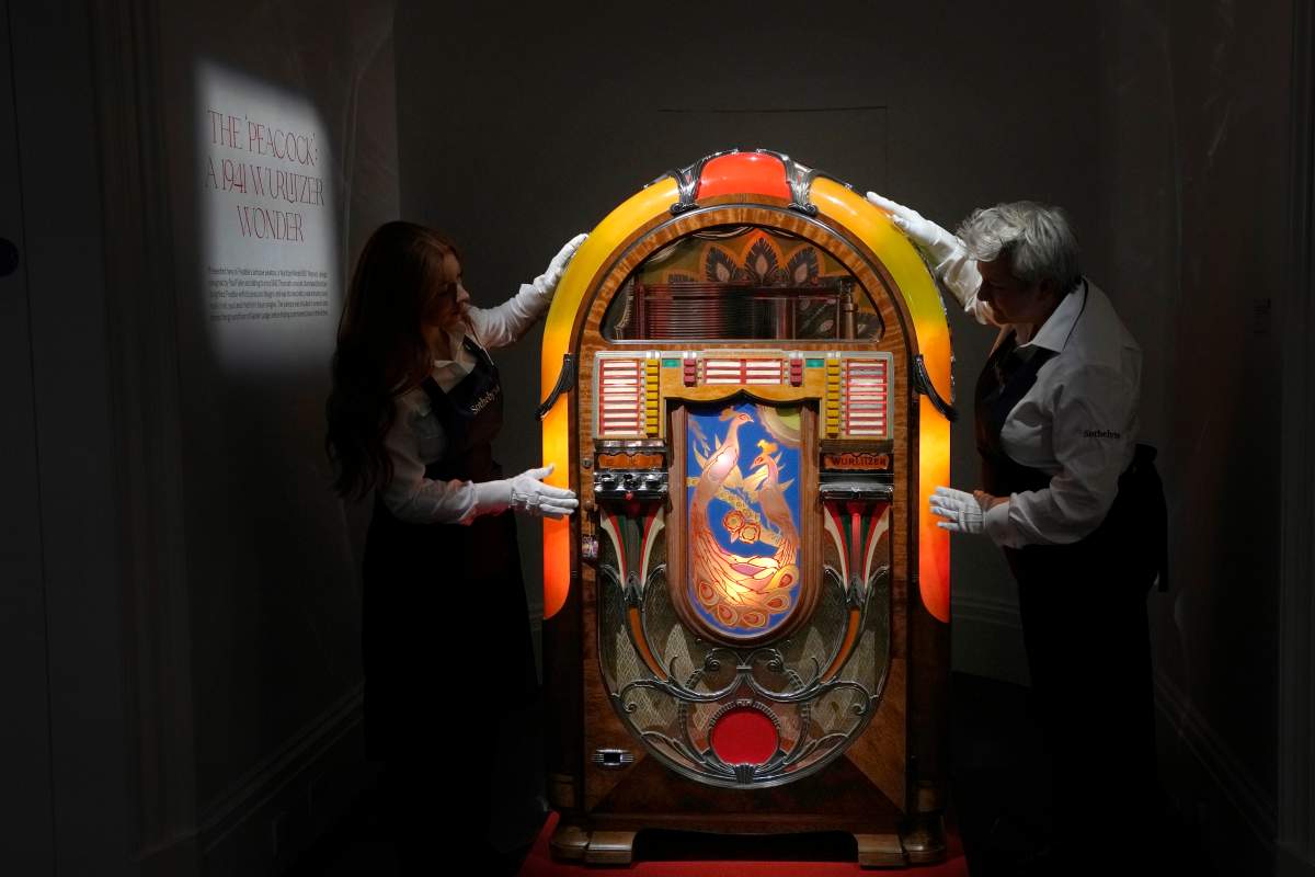 Sotheby's handlers stand with a A Wurlitzer Model 850 'Peacock' design jukebox by Paul Fuller, American, circa 1941, at Sotheby's auction rooms in London, Thursday, Aug. 3, 2023. More than 1,000 of Freddie Mercury's personal items, including his flamboyant stage costumes, handwritten drafts of “Bohemian Rhapsody” and the baby grand piano he used to compose Queen's greatest hits, are going on show in an exhibition at Sotheby's London ahead of their sale. 