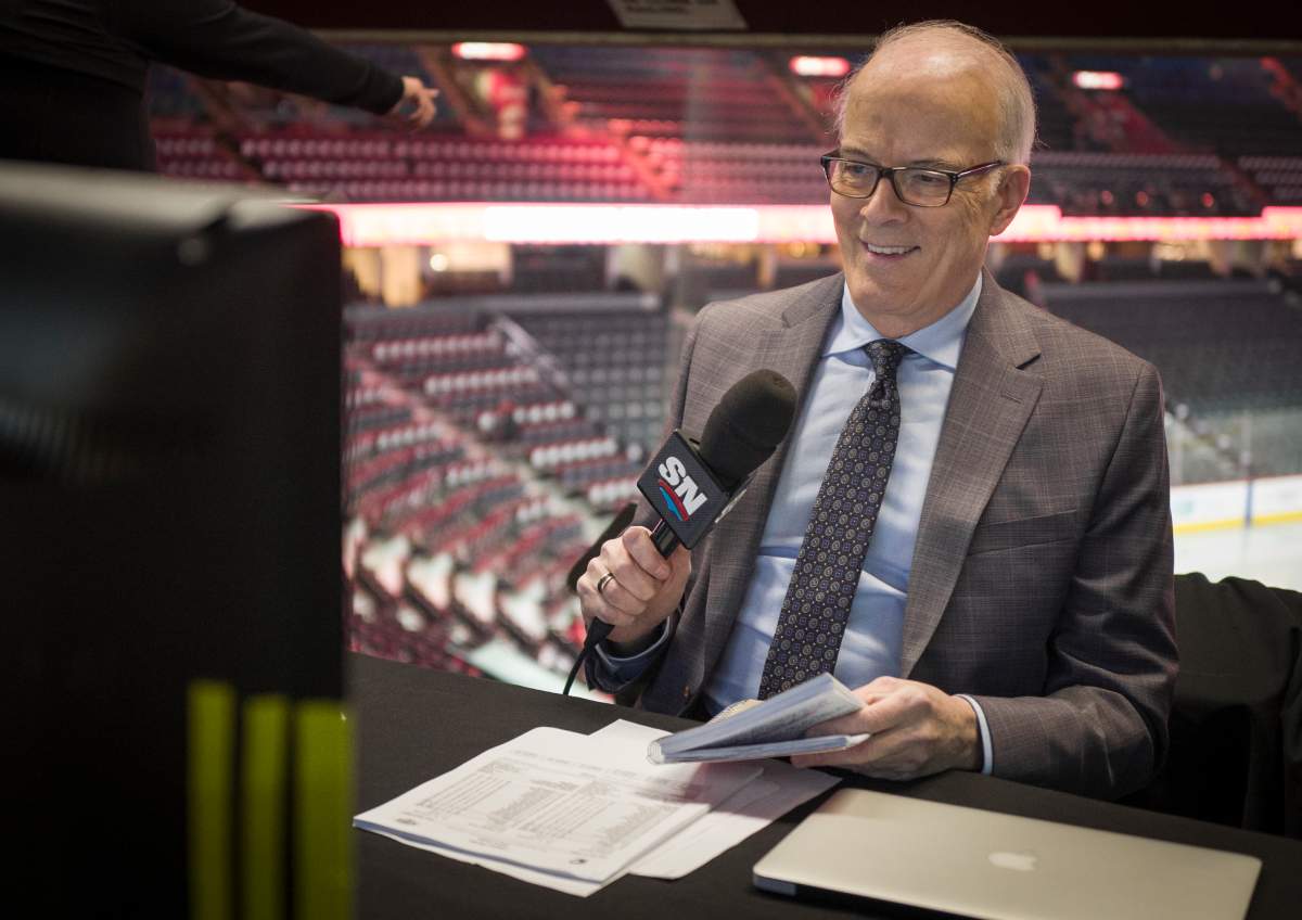 Scott Oake seated at an arena and holding a microphone