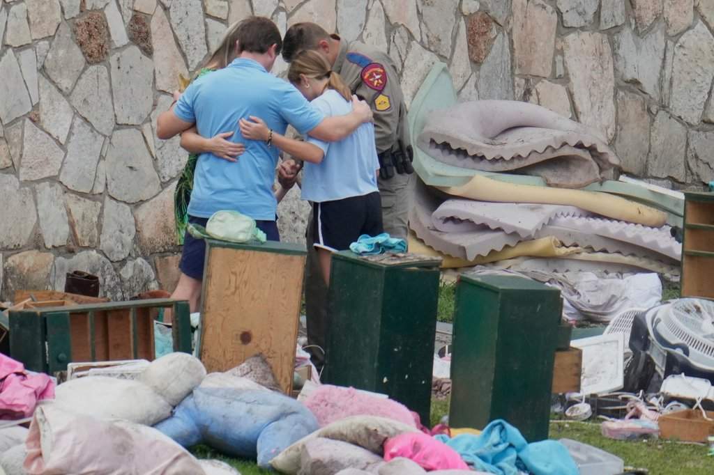 FILE - An officer prays with a family as they pick up items at Camp Mystic in Hunt, Texas on July 9, 2025.