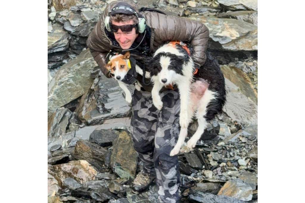 In this photo released by Precision Helicopters Ltd, Wayne Holmes holds his dog Bingo, left, after the rescue of Molly, right, at a waterfall on the Arahura River on the West Coast of the South Island of New Zealand, Tuesday, March 31, 2026.