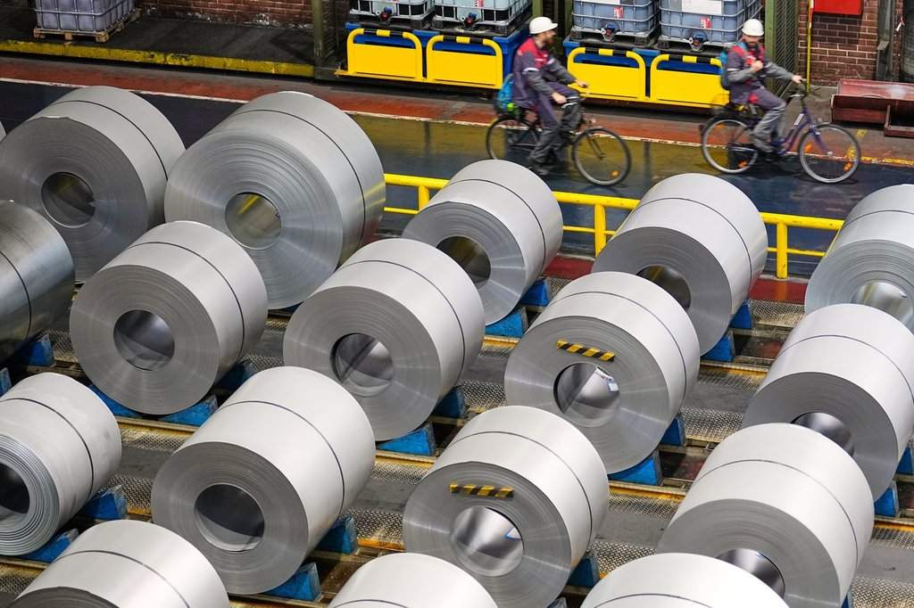 Two men drive past steel coils at the thyssenkrupp steel mill in Duisburg, Germany, Wednesday, Nov. 5, 2025. (AP Photo/Martin Meissner).