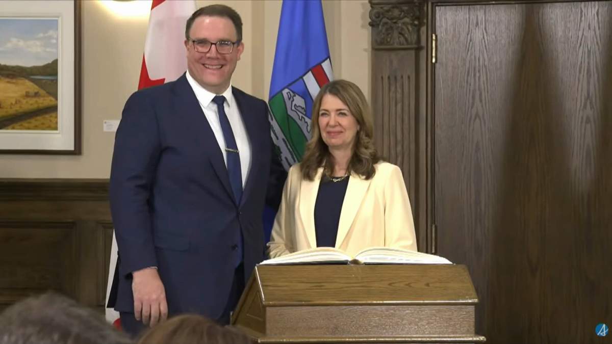 Alberta's new finance minister, Jason Nixon, and Premier Danielle Smith pose for photos after a cabinet swearing-in ceremony Thursday in Edmonton.