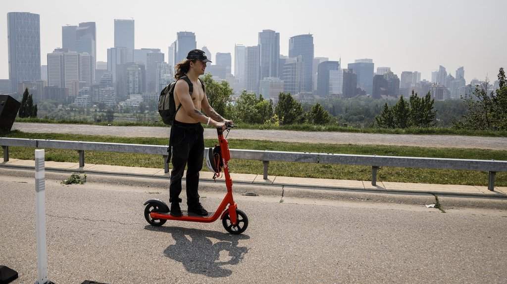 A haze of wildfire smoke from B.C. hangs over the downtown as man uses an electric scooter in Calgary on Thursday, July 15, 2021. THE CANADIAN PRESS/Jeff McIntosh.