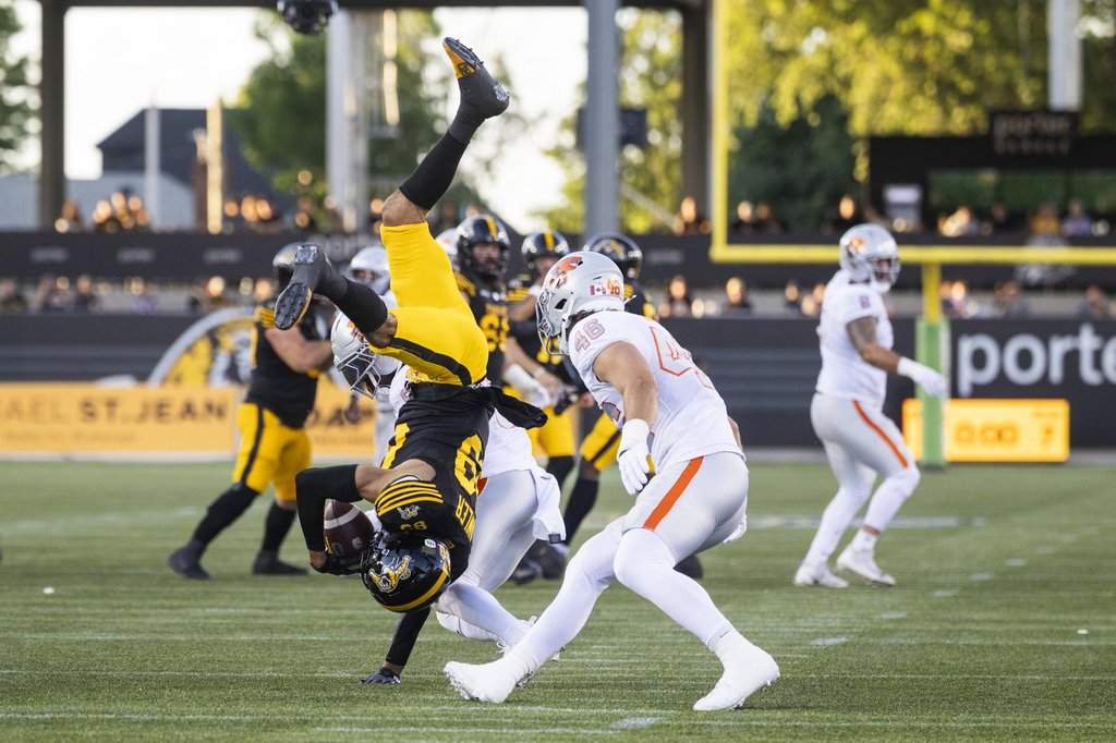 Hamilton Tiger-Cats' Kenny Lawler (89) makes a catch over B.C. Lions' T.J. Lee (back) as Ben Hladik (46) looks on during first half CFL football action in Hamilton on Friday, June 19, 2026. THE CANADIAN PRESS/Nick Iwanyshyn.