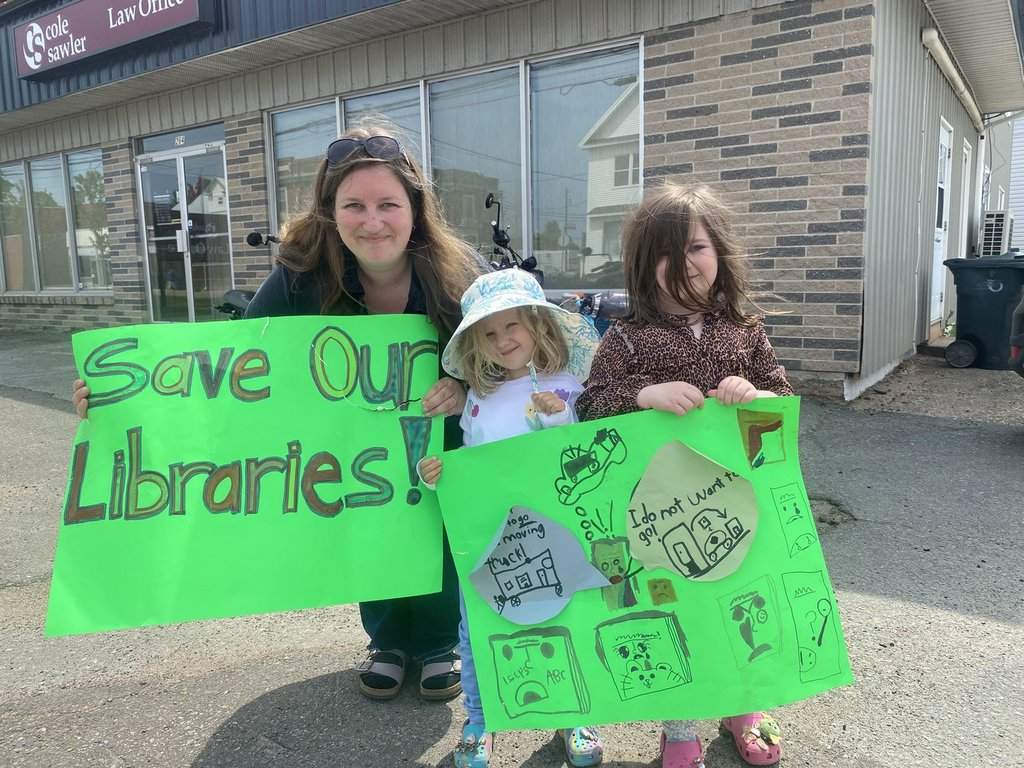 Krista Arsenault and her daughters Evie and Alice Arsenault pose with signs they made for a rally to save five rural libraries in their county that are slated to close next month, in Middleton, N.S., on Friday, June 5, 2026. THE CANADIAN PRESS/Lyndsay Armstrong.