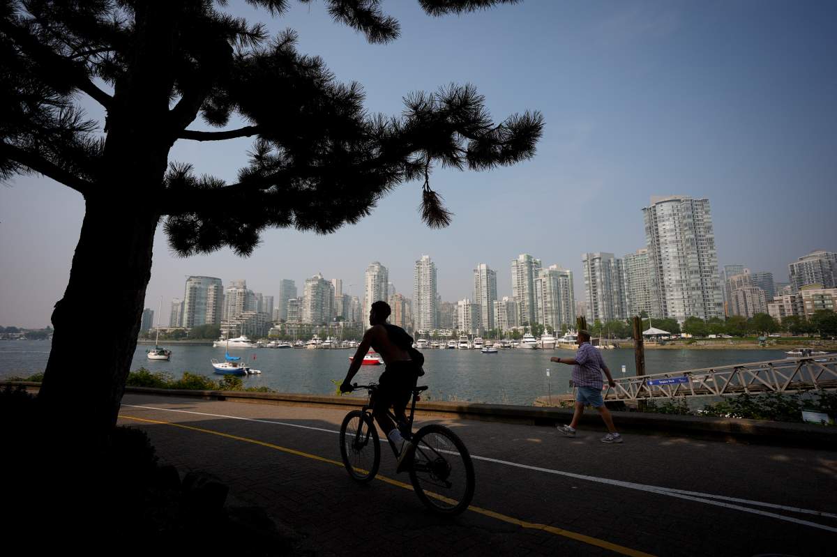 A cyclist is silhouetted while a pedestrian walks on the False Creek seawall, Wednesday, Sept. 3, 2025. 