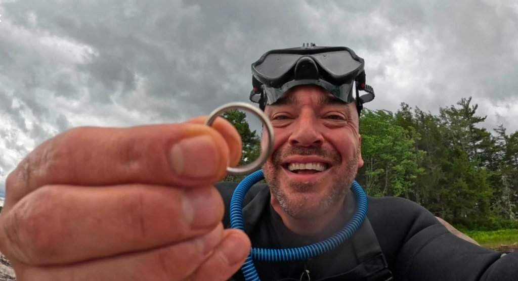 Nate McLagan emerges from a lake in Nova Scotia's Kejimkujik National Park on Saturday, June 20, 2026, in this handout photo, with the wedding ring of a Louisiana man who had lost it the weekend before. THE CANADIAN PRESS/Handout — Nate McLagan (Mandatory Credit).