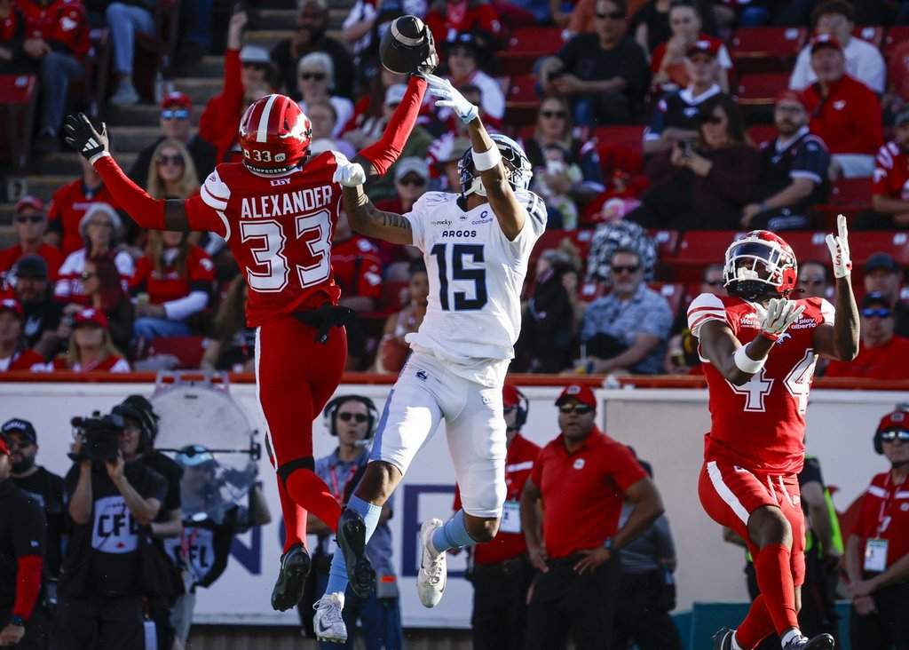 Toronto Argonauts' Makai Polk (15) reaches for a pass as Calgary Stampeders' Zy Alexander intercepts during first half CFL football action in Calgary, Thursday, July 2, 2026. THE CANADIAN PRESS/Jeff McIntosh.