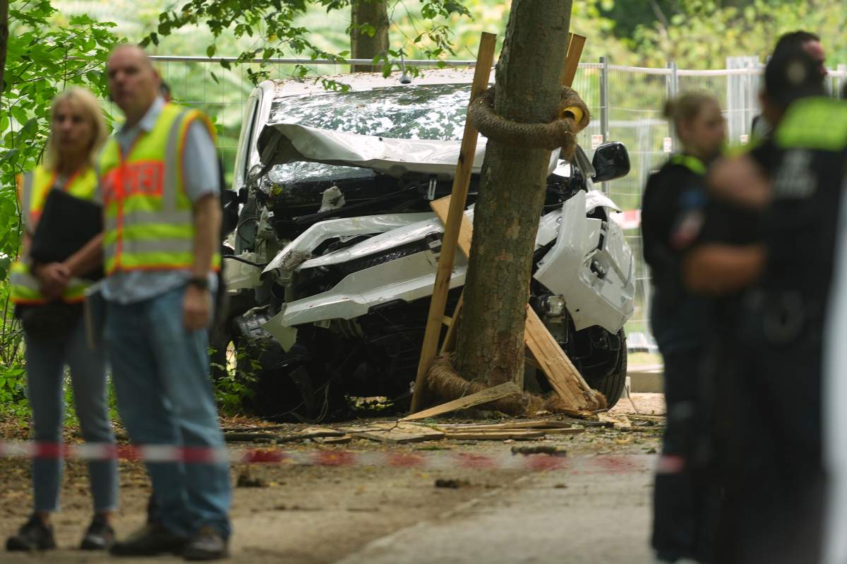 Police officers stand near a vehicle crashed into a tree after driving into a crowd near Berlin's annual Pride event, in Berlin, July 26, 2026. (AP Photo/Markus Schreiber).