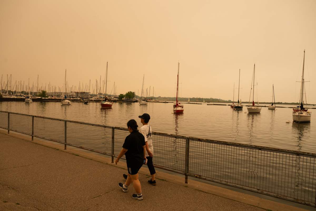 People walk on the waterfront in Toronto as wildfire smoke fills the city, on Wednesday, July 15, 2026. THE CANADIAN PRESS/Laura Proctor