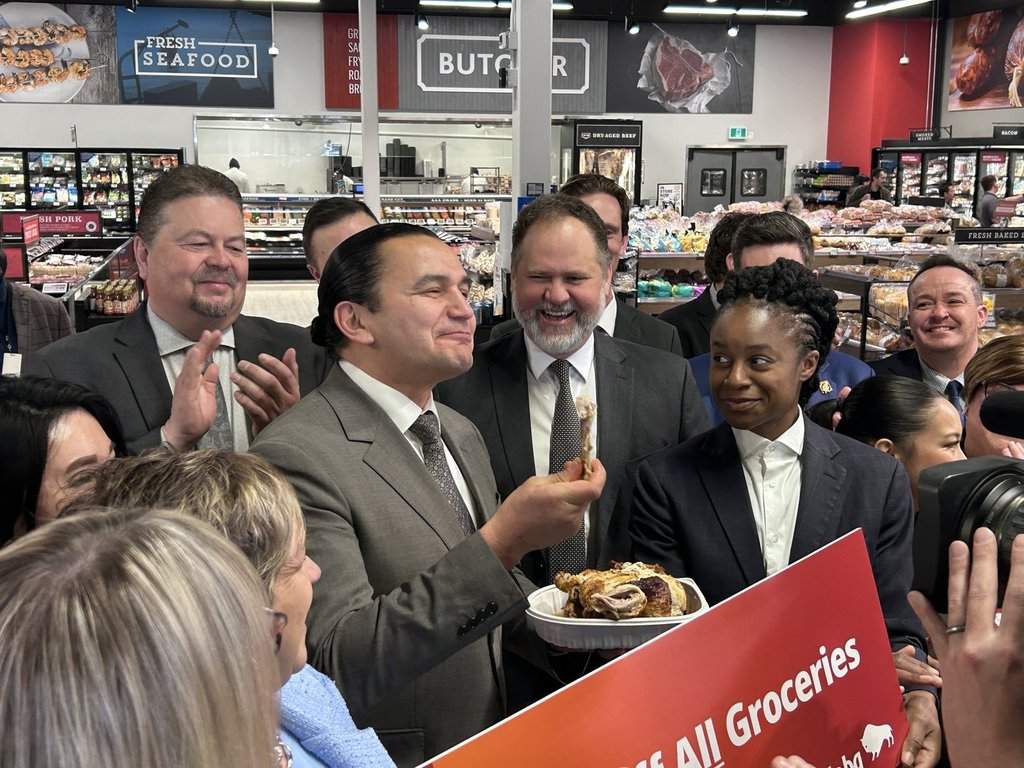 Manitoba Premier Wab Kinew eats rotisserie chicken at a news conference inside a grocery store in Winnipeg, on Wednesday, March 25, 2026. Kinew was promoting his government's plan to remove the provincial sales tax from all food in grocery stores. 