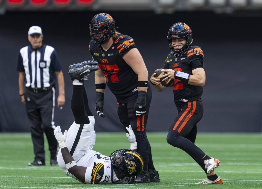 B.C. Lions quarterback Nathan Rourke (right) looks to run after teammate Chris Schleuger (centre) knocks down Hamilton Tiger-Cats' Mario Kendricks Jr. with a block during first half of CFL action in Vancouver on Saturday, Aug. 8, 2026. THE CANADIAN PRESS/Rich Lam.