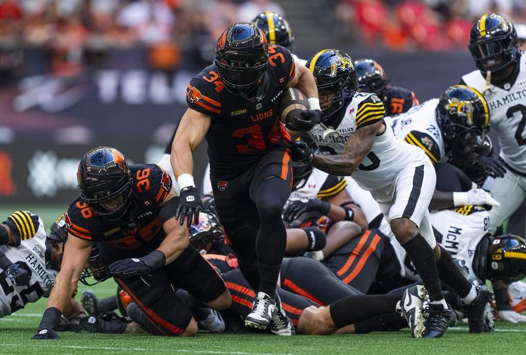B.C. Lions' Zander Horvath (centre) runs by Hamilton Tiger-Cats' Devodric Bynum during first-half CFL action in Vancouver on Saturday, August 8, 2026. THE CANADIAN PRESS/Rich Lam.