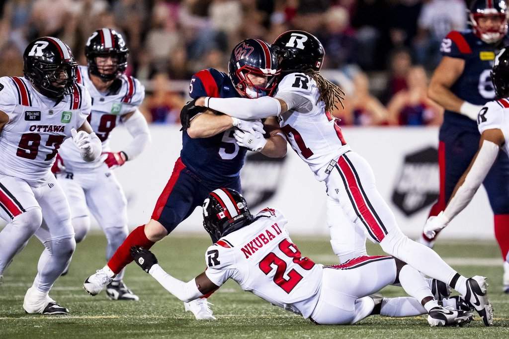 Montreal Alouettes' Travis Theis (5) is tackled by Ottawa Redblacks' King Ambers (27) and Shadwel Nkuba II (28) during CFL action in Montreal on Aug. 20, 2026. THE CANADIAN PRESS/Christopher Katsarov.