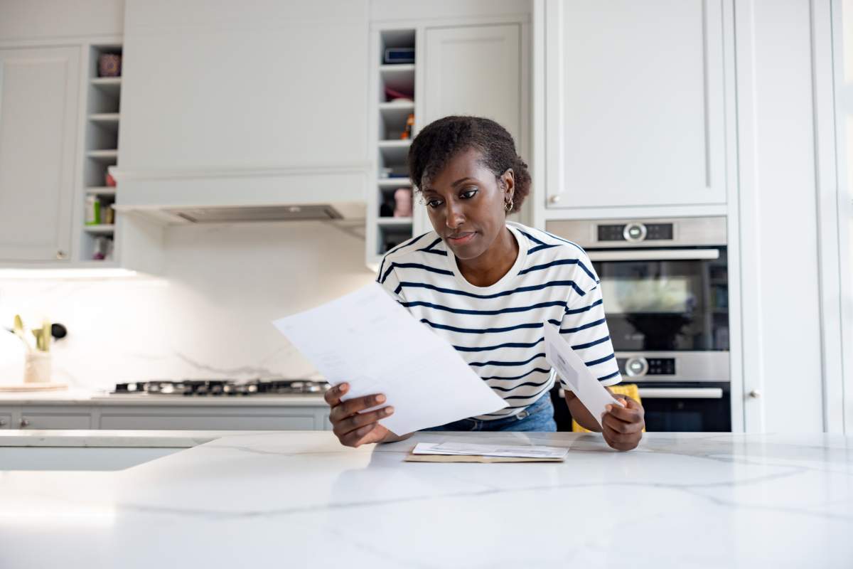 African American woman at home reading a letter in the mail at her kitchen and looking a bit worried - lifestyle concepts.