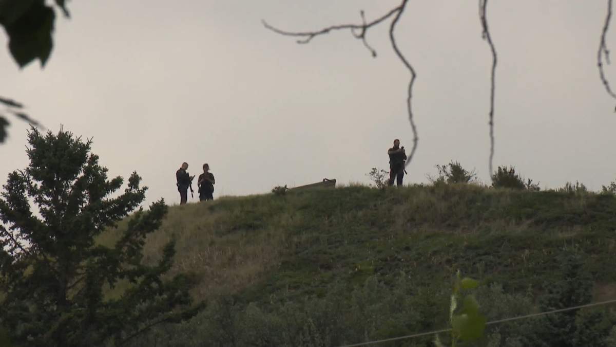 Several heavily armed police officers are seen on a hill overlooking Edworthy Park during the search for a man who shot a police officer during a nearby traffic stop on Monday.