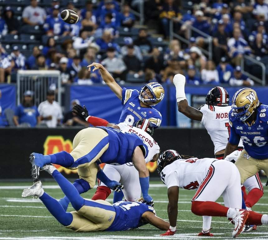 Winnipeg Blue Bombers quarterback Zach Collaros (8) gets the throw away as he is grabbed by Ottawa Redblacks Jelani Stafford (97) during first half CFL action in Winnipeg on Friday, Aug. 14, 2026. THE CANADIAN PRESS/John Woods.