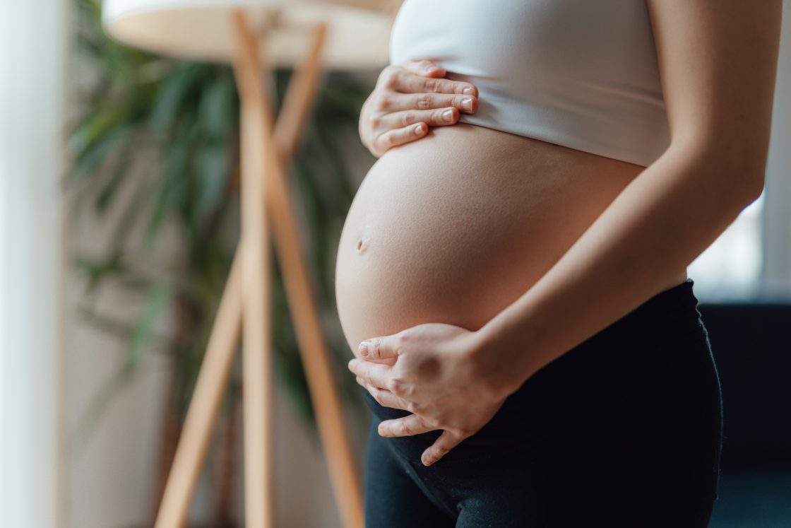 Side view close-up of pregnant woman touching her belly. 