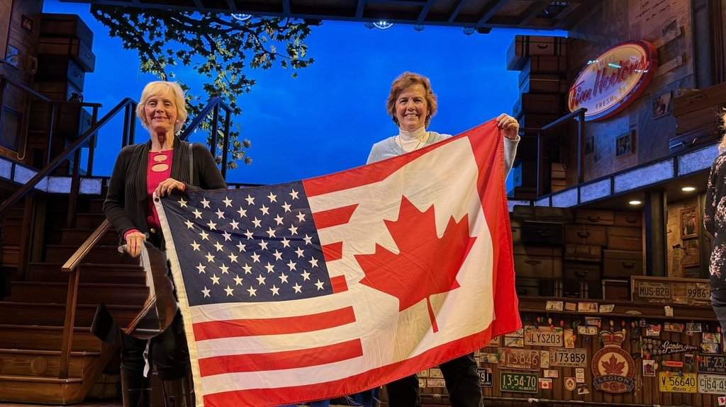 Sue Riccardelli, right, and her wife Maureen Murray are shown in this undated handout photo holding up their special Canadian and American flag after a local production of "Come From Away" in New Jersey. THE CANADIAN PRESS/Handout — Laura Giostra (Mandatory credit).
