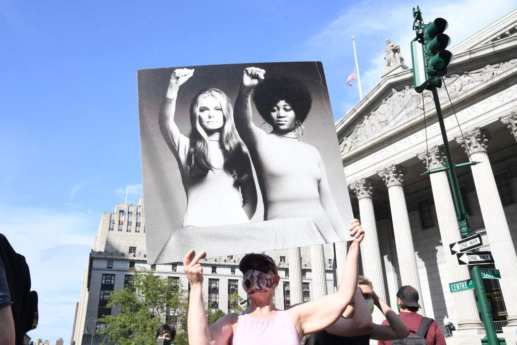 A protester holds a poster that shows an image of Gloria Steinem and Dorothy Pitman Hughes sharing a large skirt, each with a raised fist salute to demonstrate feminist solidarity, during a rally against the killing of George Floyd at Foley Square on May 29, 2020 in New York City. 
