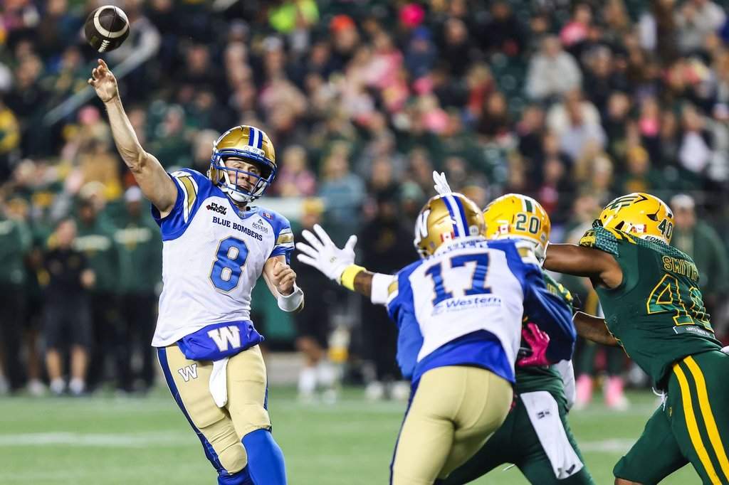 Winnipeg Blue Bombers quarterback Zach Collaros (8) throws a pass under pressure from Edmonton Elks' Kenny Logan Jr. (20) and Robbie Smith (40) during first-half CFL football action in Edmonton on Friday, Oct. 16, 2026. THE CANADIAN PRESS/Codie McLachlan.