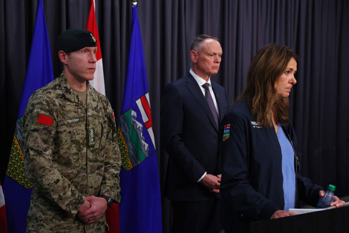 Commander of the 1st Canadian Division, Major-General L. W. Rutland, left, and National Defence Minister David McGuinty, centre, listen as Alberta Premiere Danielle Smith addresses the fatal incident at CFB Wainwright in Alberta, in Edmonton, Sunday, Oct. 18, 2026.