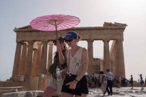 FILE - Tourists with an umbrella walk in front of the Parthenon at the ancient Acropolis in central Athens. (AP Photo/Petros Giannakouris, File)
