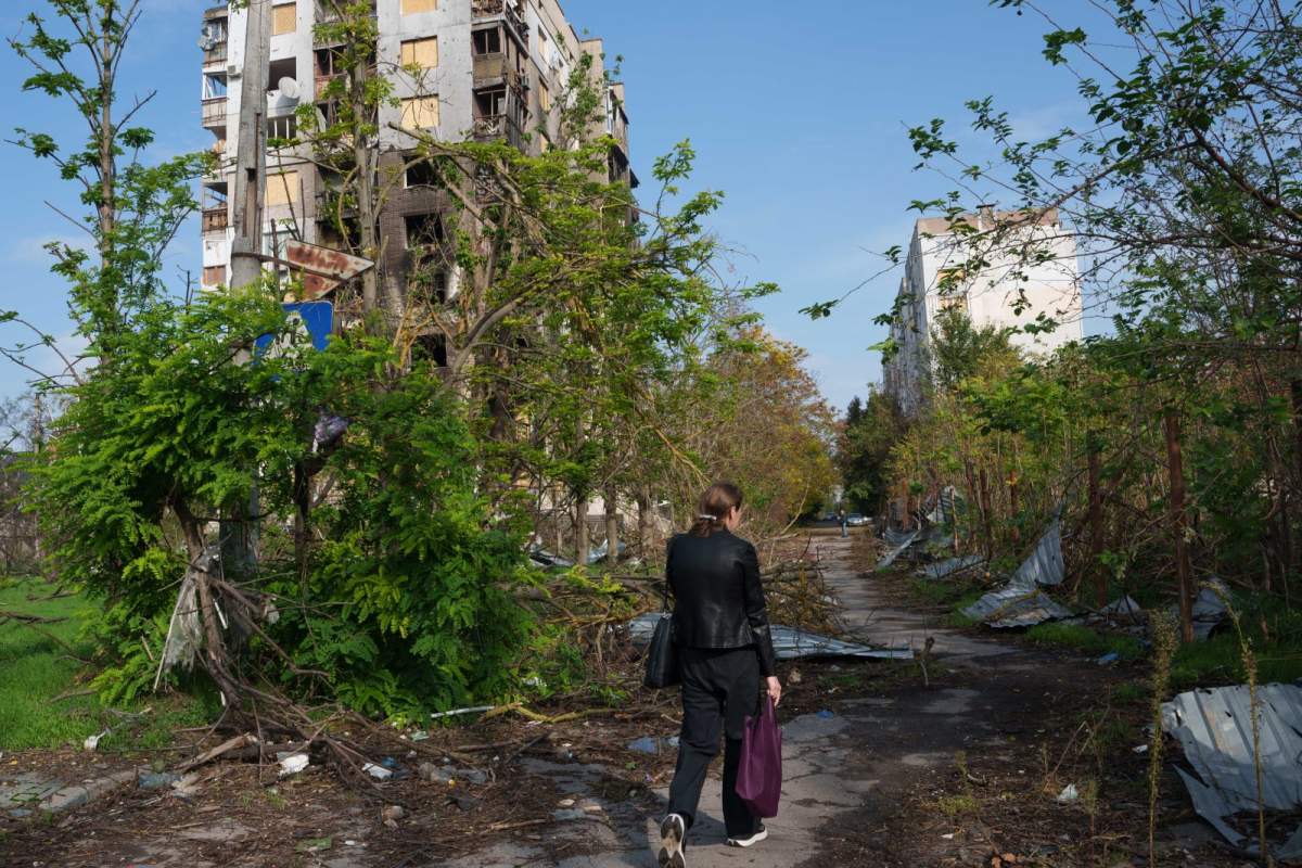 A woman walks in front of a residential building damaged in a Russian attack during a local ceasefire related to a humanitarian aid mission in Oleshky, in Kherson, Ukraine, Wednesday, Oct. 28, 2026. (AP Photo/Evgeniy Maloletka).