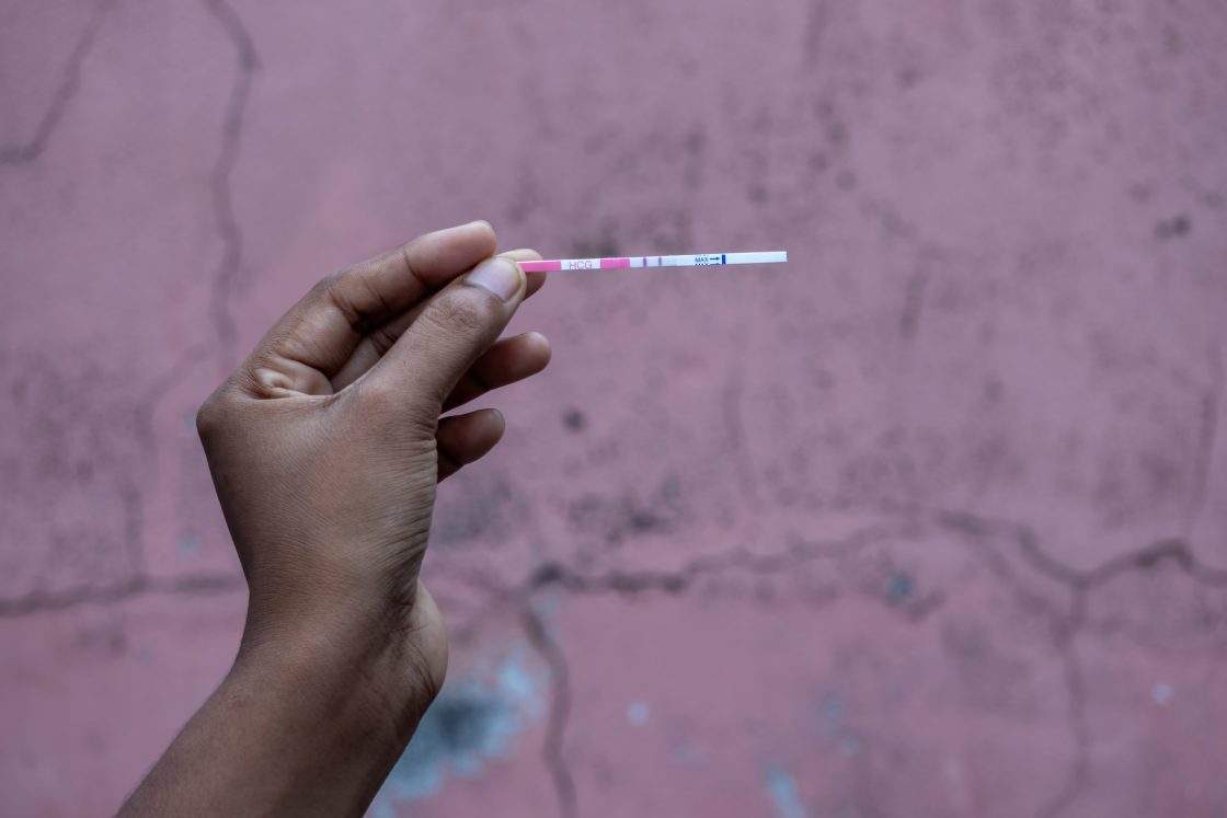 Close-up of a female hand holding a positive HCG pregnancy test strip with two distinct lines.