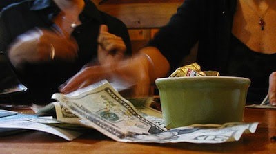 Two people sorting cash—perhaps in their peak earning years—leave money near a green bowl at a restaurant table.