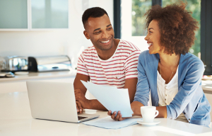 Shot of a smiling young couple going over their paperwork and using a laptop